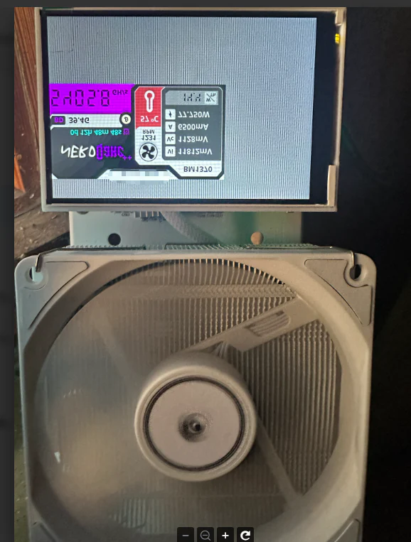 Close-up of a computer cooling system with a digital display showing system information like temperature (21°C) and voltage (VmStart, Vm8t). The fan dominates the view.